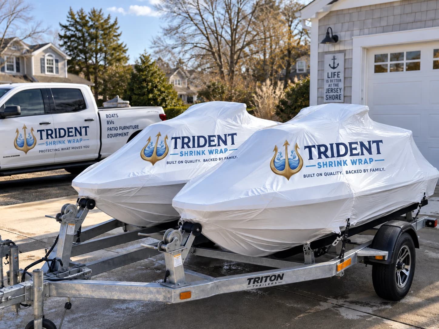 Two personal watercraft wrapped in white film on a double trailer in a driveway